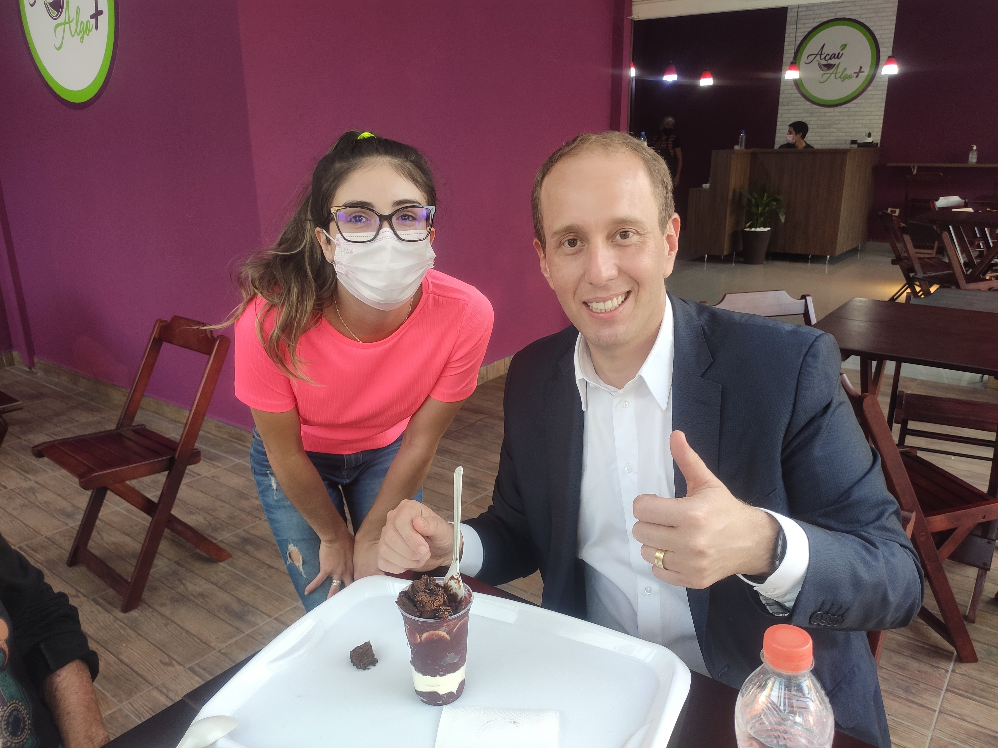 Prefeito de Sorocaba Rodrigo Manga visitando a loja Açaí Algo Mais em 2022, sentado à mesa com uma atendente e um copo de açaí
