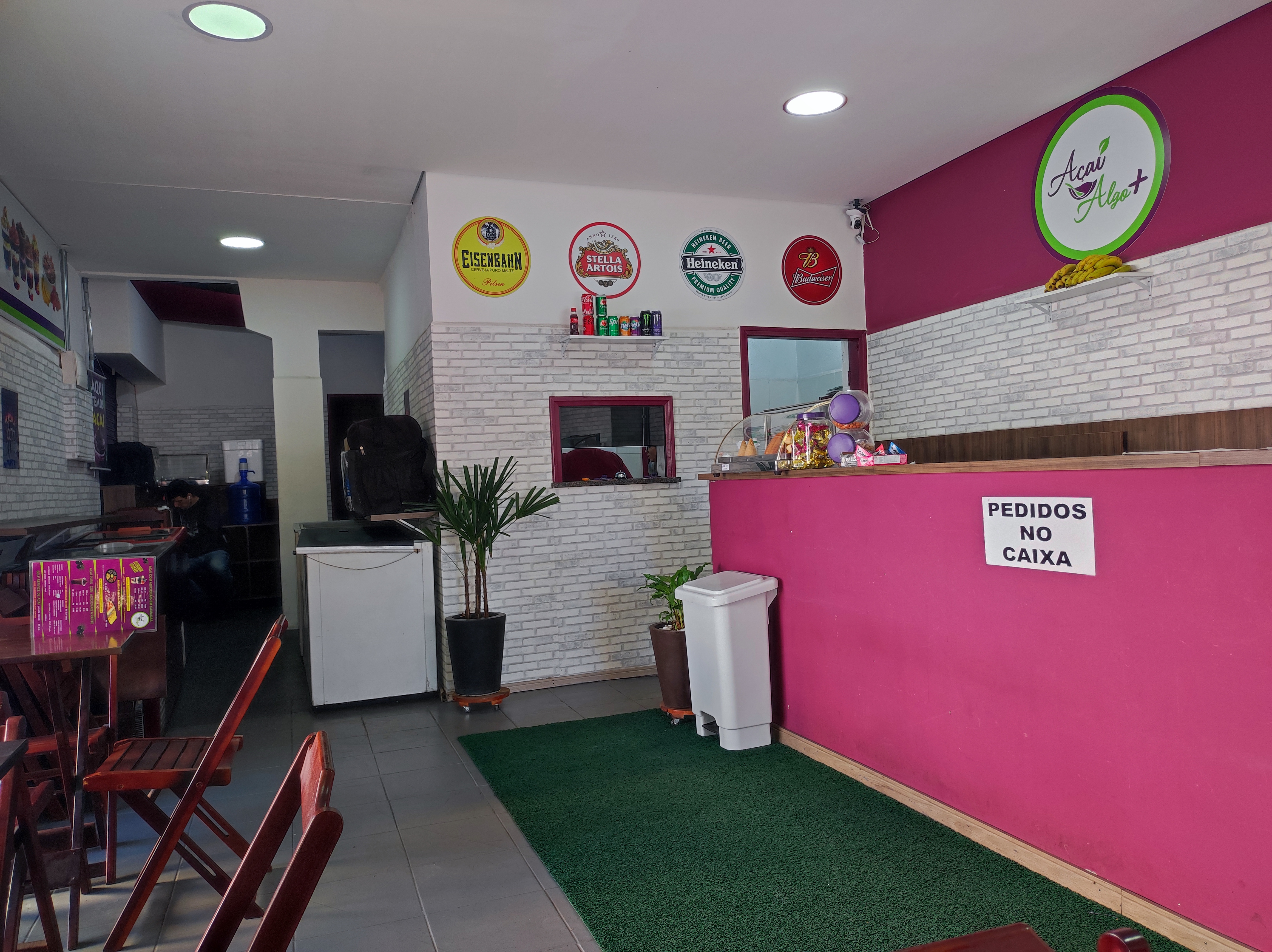 Salão da Açaí Algo Mais em Sorocaba, com paredes brancas em tijolo aparente, parede pink com logo circular, mesas de madeira e identidade visual consolidada